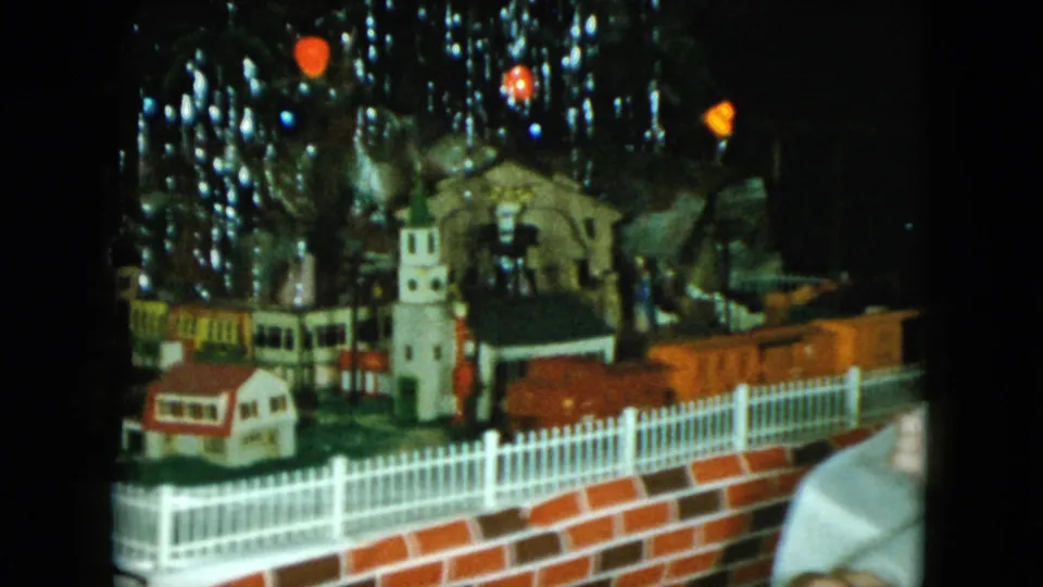 A 1951 Cleveland home-movie frame shows orange train cars in a tabletop miniature railroad scene with holiday decorations behind them.