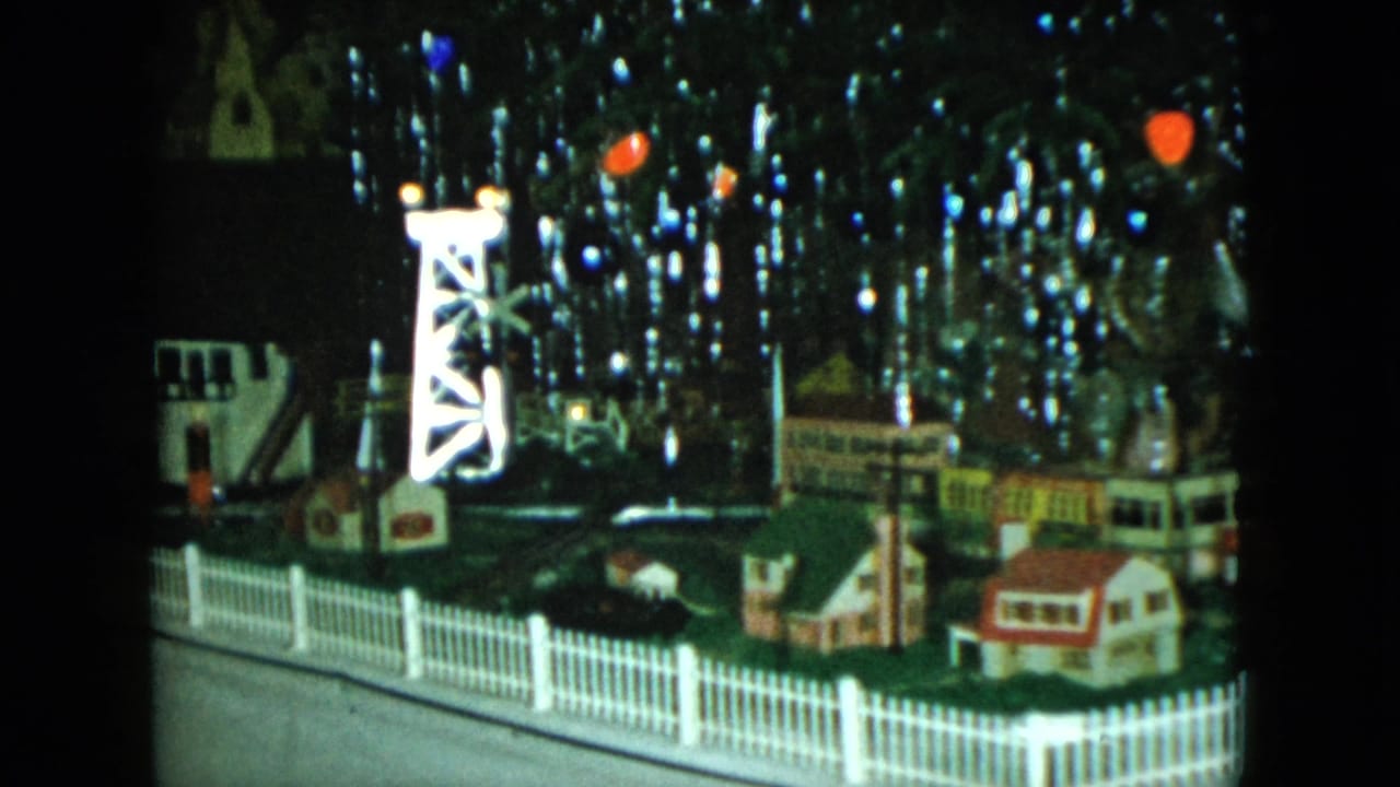 Miniature rail scene with a bright tower, small buildings, fence, track, and shiny reflections.