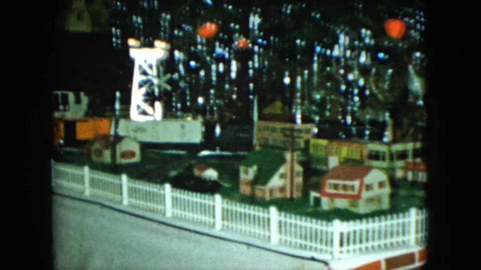 The final sampled frame shows more of the 1951 Cleveland holiday layout, including small houses, a white fence, a tower, and glowing tree lights.