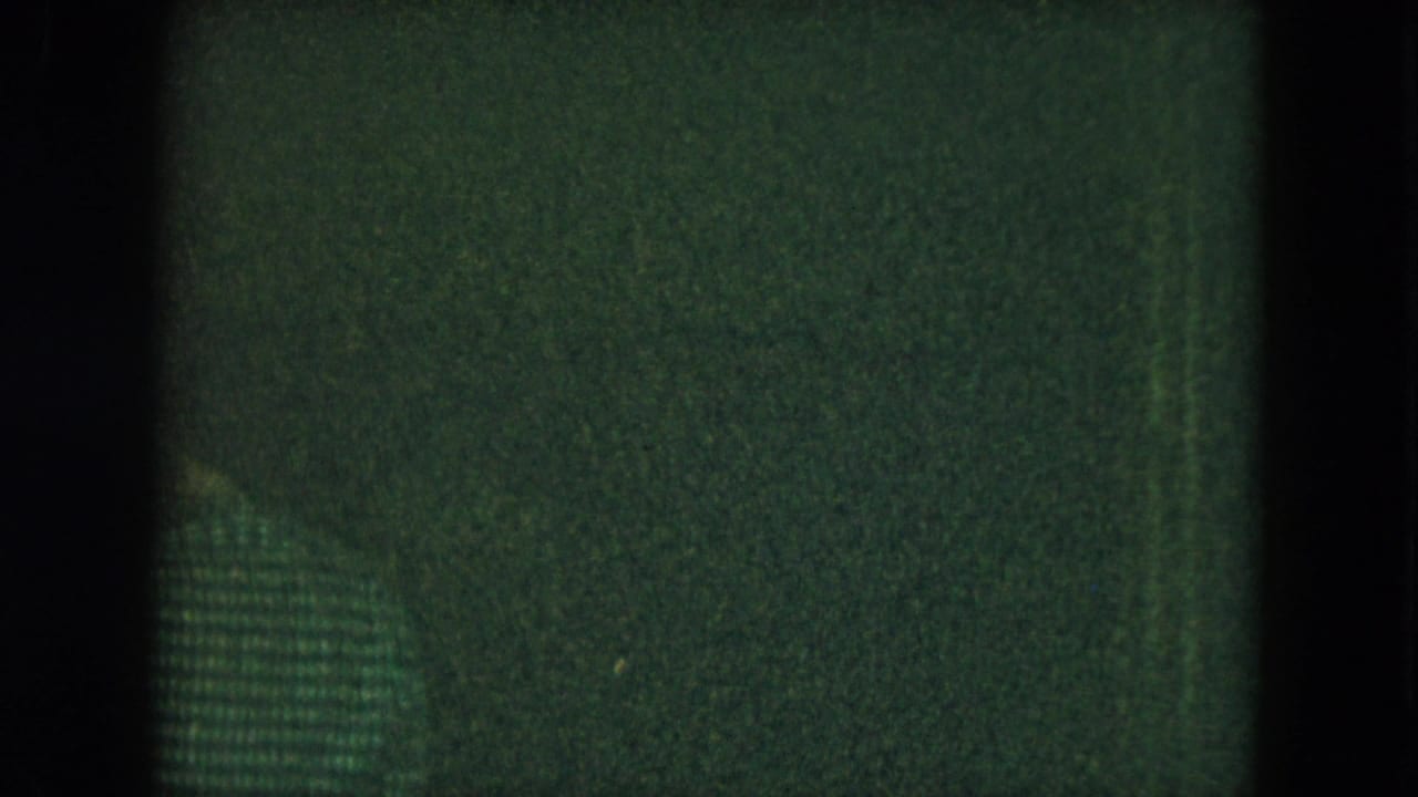 Low-light 1951 Cleveland nightclub frame with green cast, grain, vertical shadows, and a faint patterned patch near the center.