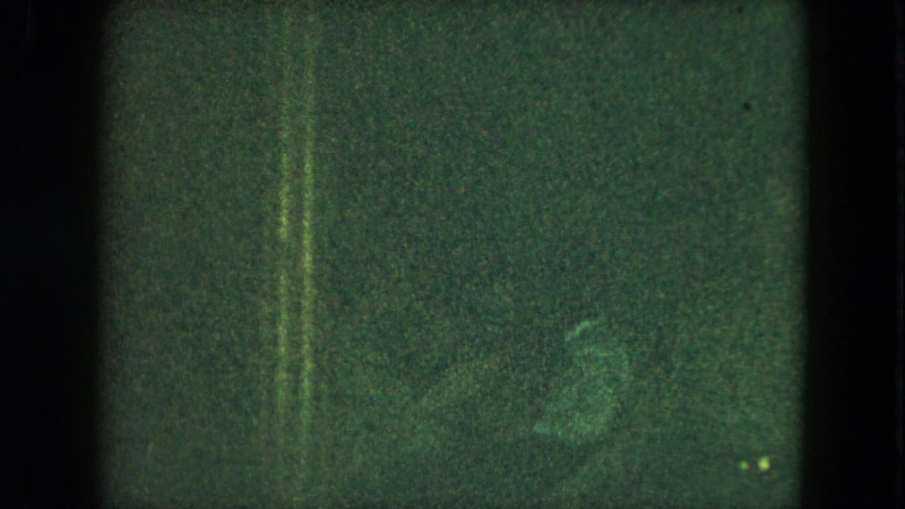 Underexposed 1951 Cleveland 8mm frame with green cast, film grain, scratches, and indistinct forms in a dark party setting.