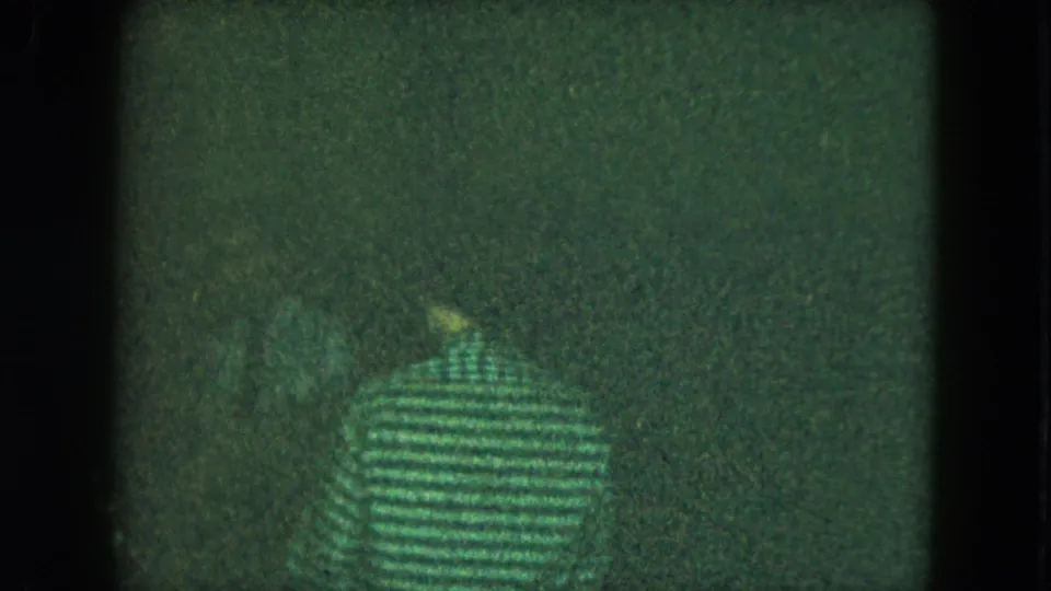 A person in a striped shirt appears from behind in a dim 1951 Cleveland party scene, surrounded by darkness, grain, and film scratches.