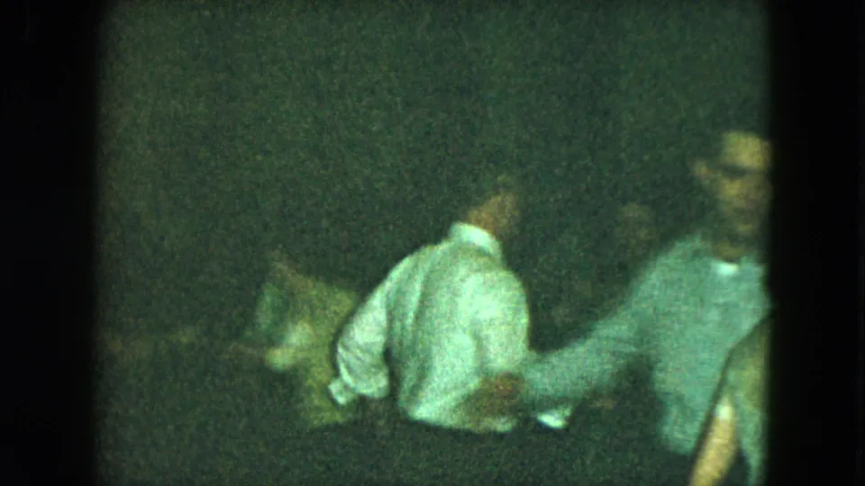 Several people are visible in a dark 1951 Cleveland party frame, including a central figure in a light shirt and another figure at right.