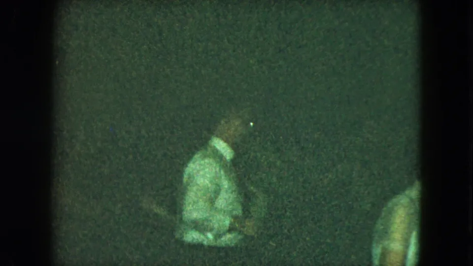 Dim 1951 Cleveland home-movie frame with a man in a light shirt and tie partly visible in a crowded indoor dance setting.