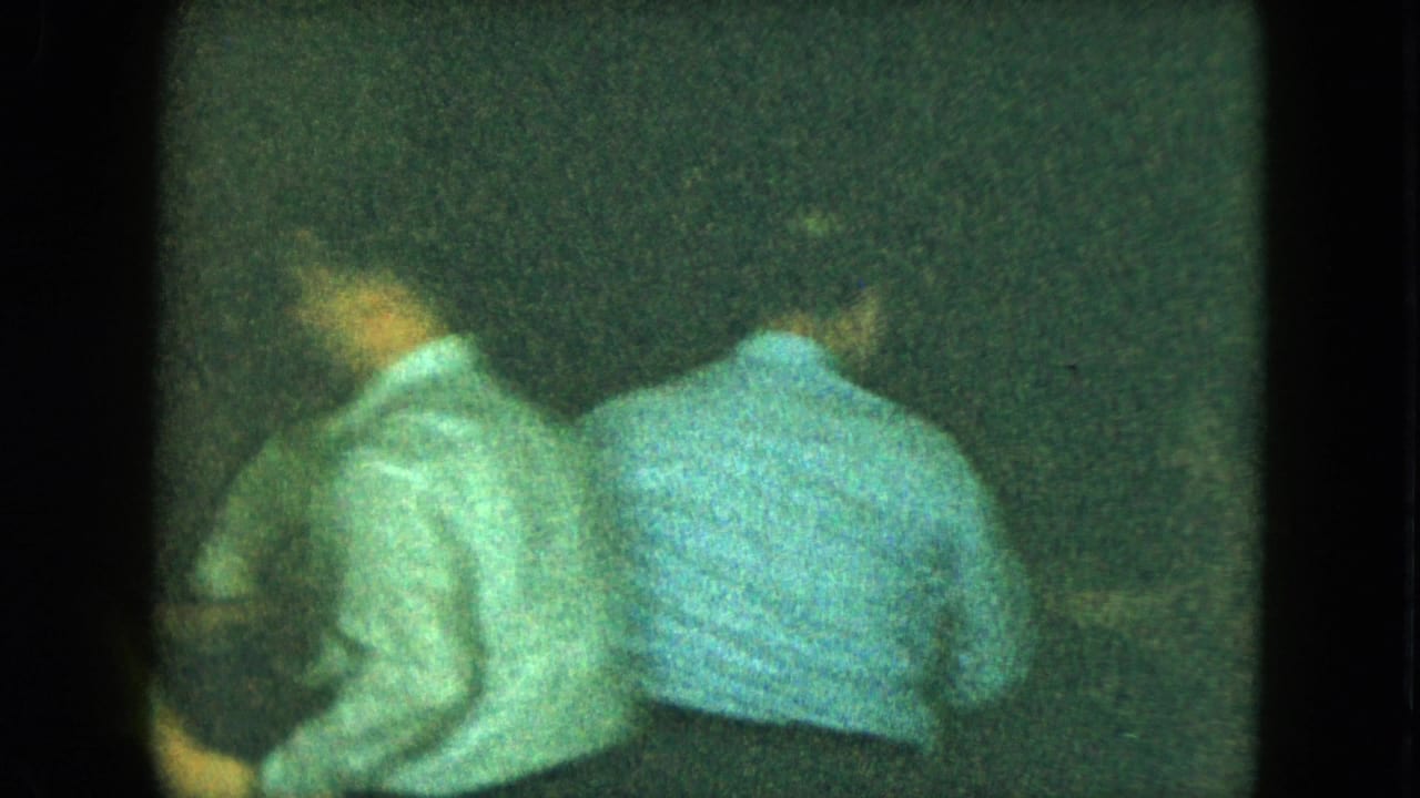 Two adults in light shirts appear to lean or dance together in the 1951 Cleveland party footage, seen through heavy grain and low light.