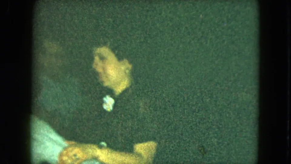A woman in dark clothing, with a small light detail near her collar, sits or turns beside another adult in the Cleveland party scene.