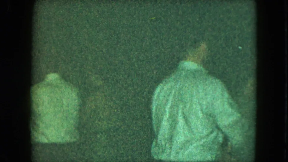 1951 Cleveland 8mm frame showing two men from behind in light shirts against a dark interior background.