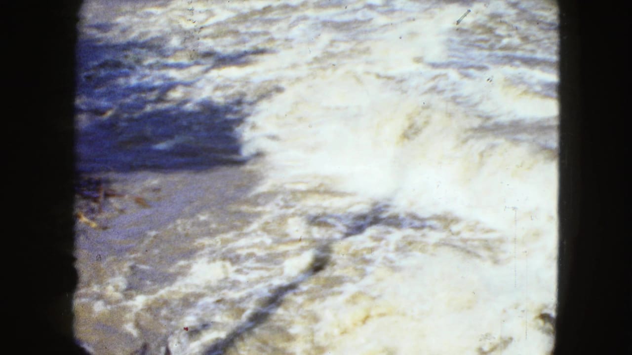 1951 Cleveland 8mm frame showing churning water beside a wooded shoreline, with debris partly visible along the bank.