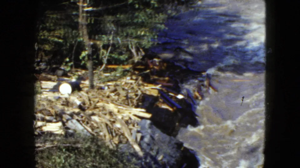 1951 Cleveland 8mm frame showing broken branches and logs piled along a wooded bank next to turbulent water.