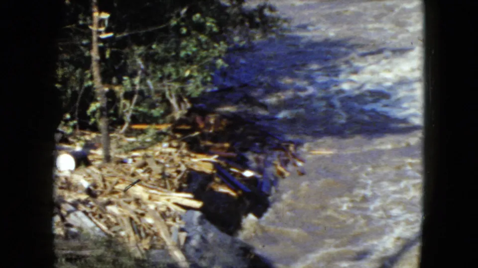 1951 8mm Cleveland-area river view with fallen logs and bank debris beside fast, foaming water.