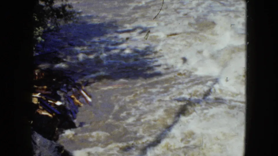 1951 8mm frame near Cleveland showing churning river water and white foam beside a dark, wooded shoreline.
