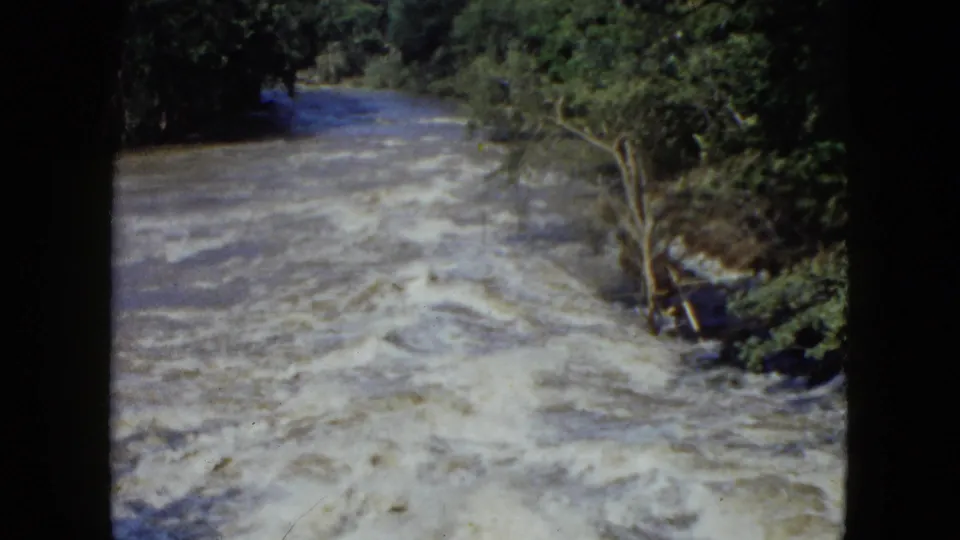 1951 Cleveland-area 8mm view of rough river current, foamy water, and trees along the right bank.