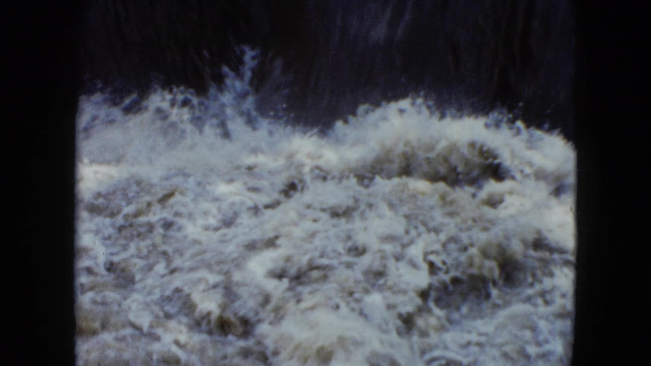 Churning white water fills the frame below a dark bank.
