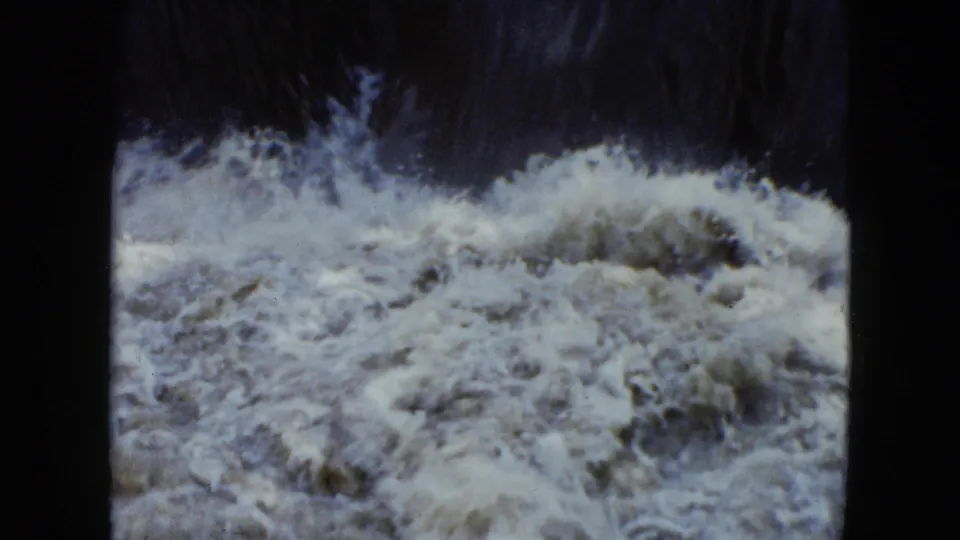 1951 Cleveland, Ohio 8mm frame of turbulent rapids rolling beneath a dark, shadowed water edge.