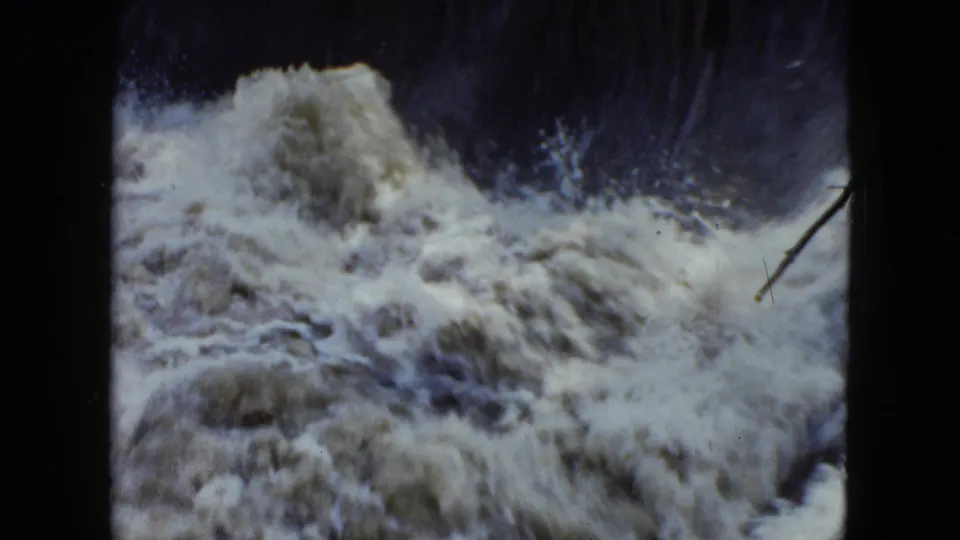 1951 Cleveland home-movie footage shows a breaking wave of floodwater, spray, and a small branch or debris near the right side.