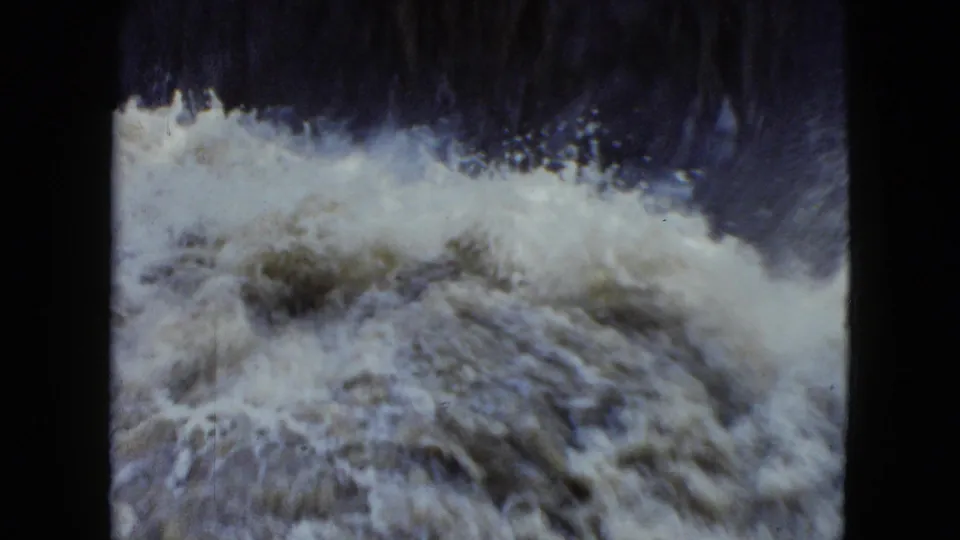 The final 8mm frame shows foamy, muddy floodwater rolling below a dark channel edge in the Cleveland 1951 clip.