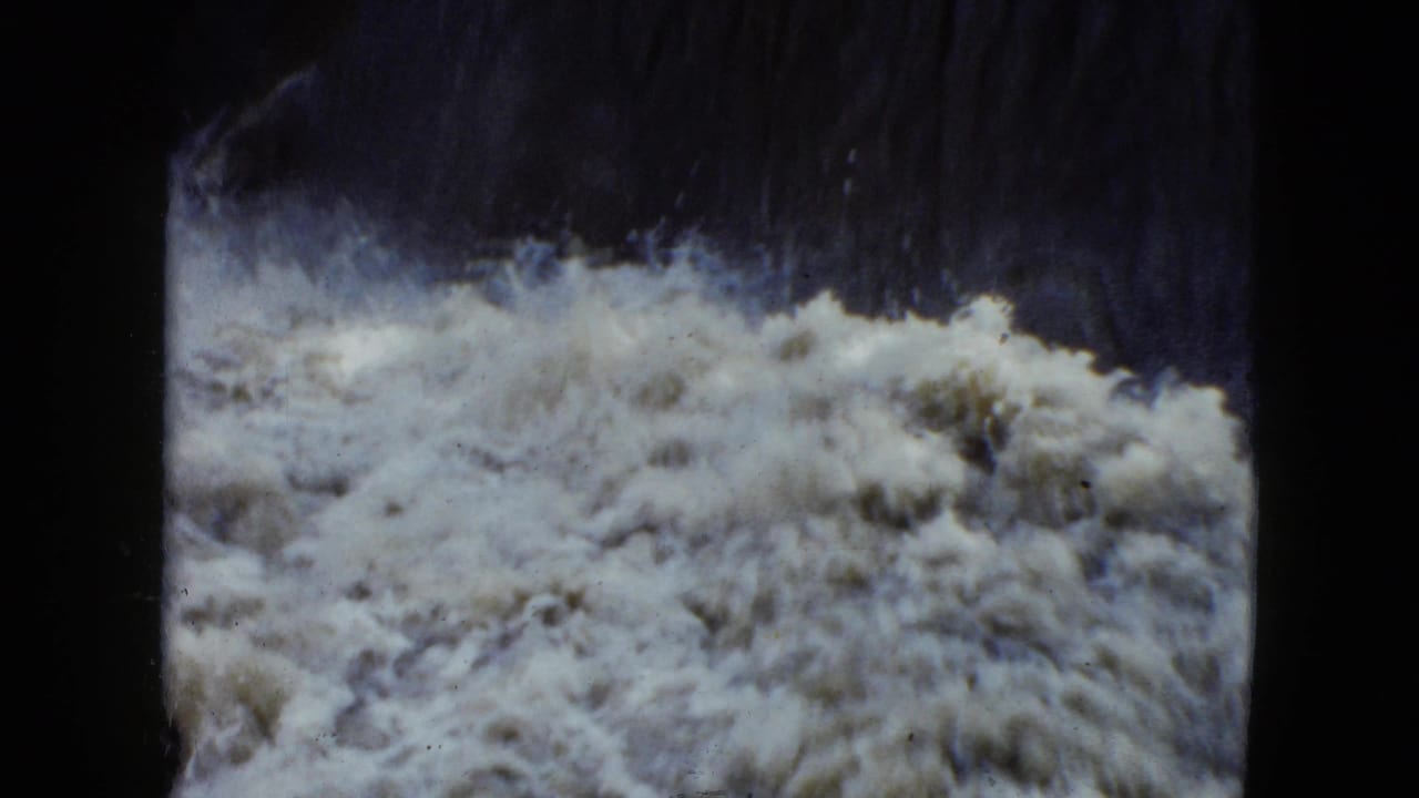 Close 1951 8mm view of white froth and churning water beneath a shadowed small waterfall in Cleveland, Ohio.