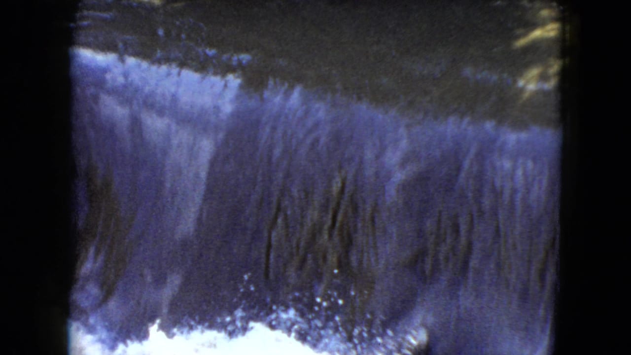 1951 Cleveland-area 8mm frame showing water spilling over a low dam or spillway beneath dark trees and brush.