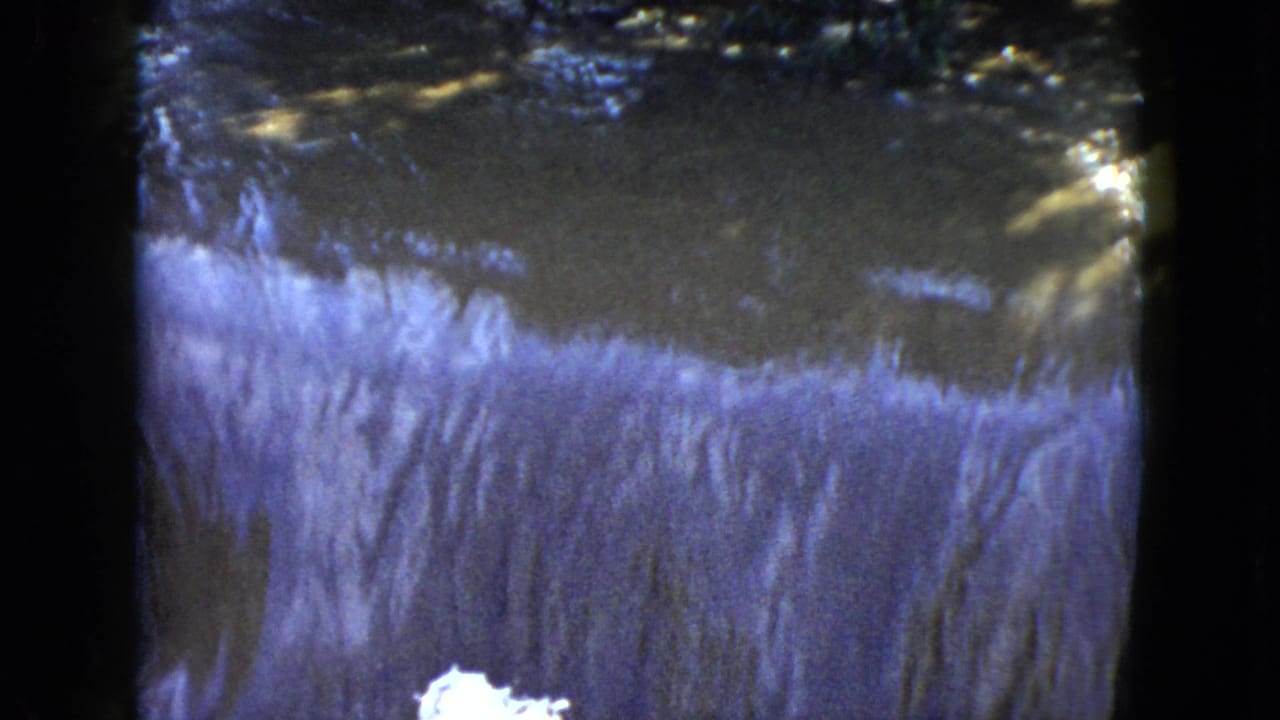 A similar view of water cascading over a low edge with trees and brush in the background.