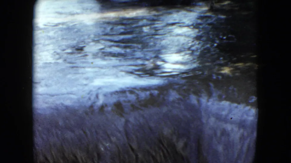 1951 Cleveland-area 8mm frame of bright rippling water and a shaded wooded bank just before a waterfall.