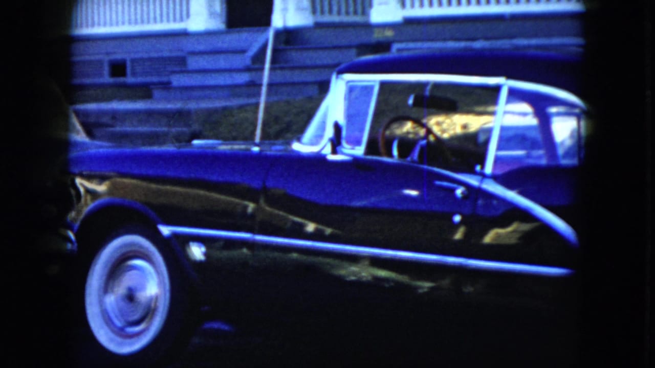 Black vintage convertible parked along a street with chrome trim and a whitewall tire.