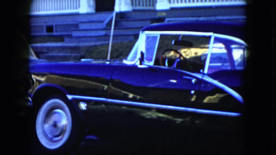 A black mid-century convertible is parked on a Cleveland street, showing chrome side trim, whitewall tire, and a porch in the background.
