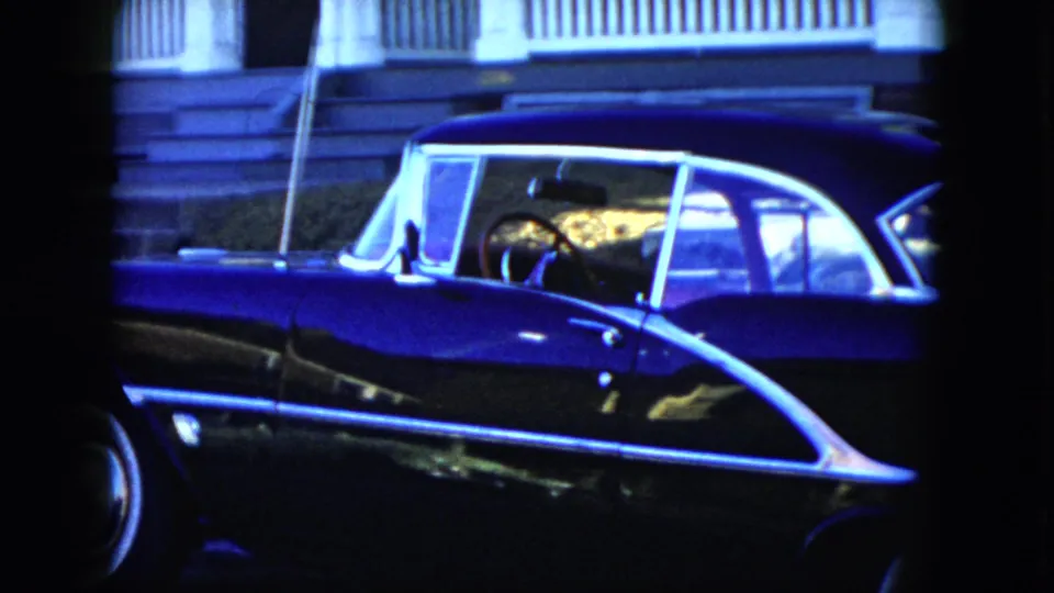 The 1951 Cleveland footage lingers on the side of a black convertible, with white roof framing, chrome trim, and residential porch details behind it.