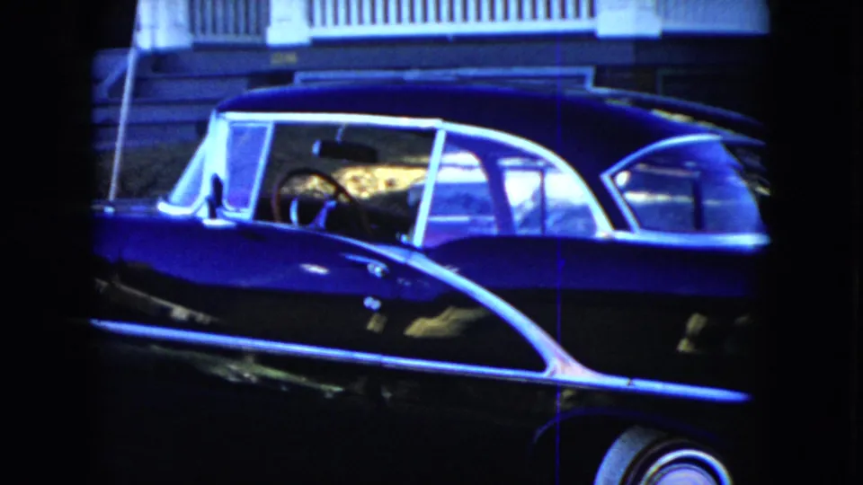 A close home-movie view shows the black convertible's side and rear section, including chrome trim, white roof framing, and a whitewall tire.