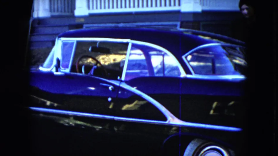 1951 Cleveland home-movie frame of a dark blue sedan with chrome trim parked near a porch railing.