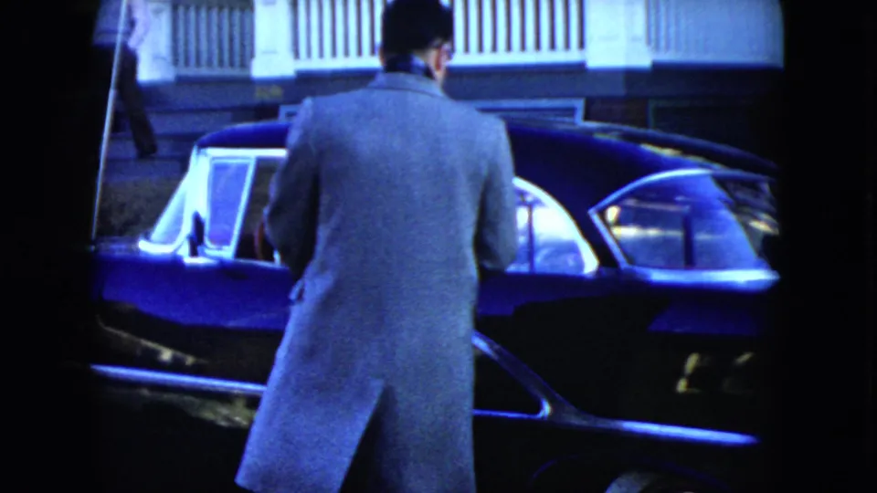 The man stands near the driver's side of the dark blue sedan, seen from behind in a 1951 Cleveland home-movie frame.
