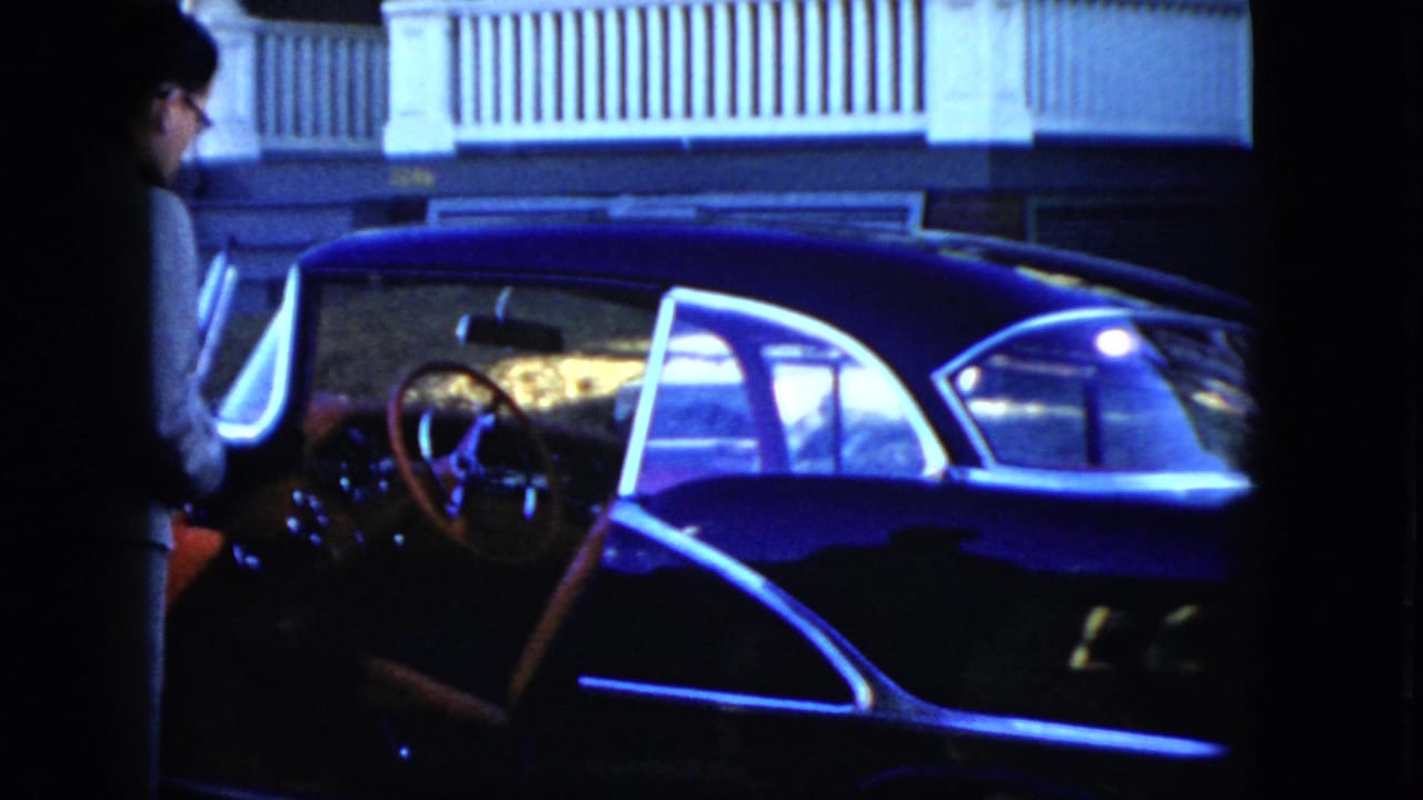 In Cleveland, Ohio, 1951 home-movie footage, a man stands beside an open dark sedan door at night with the steering wheel visible.