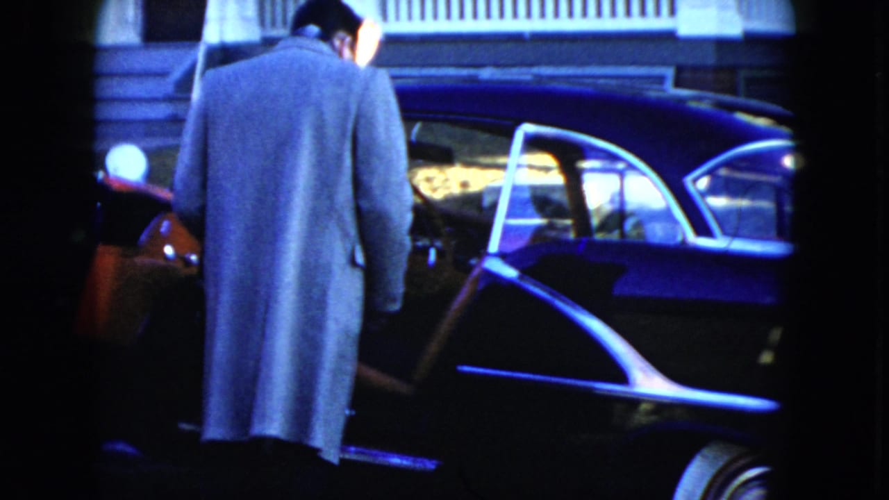 In Cleveland, Ohio, 1951 home-movie footage, a man in a light overcoat stands by a dark sedan with an open door.