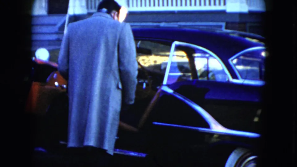 In Cleveland, Ohio, 1951 home-movie footage, a man in a light overcoat stands by a dark sedan with an open door.