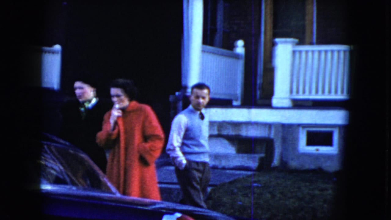 Three adults stand near a parked car in front of a house porch.