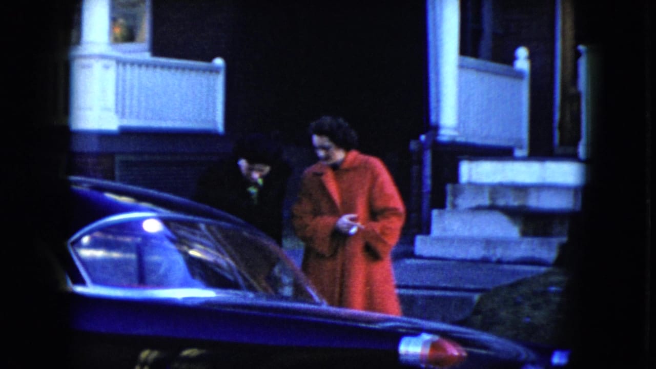 In Cleveland, Ohio, 1951, a woman in a red coat and a man in dark clothing stand near a dark car outside a porch at night.