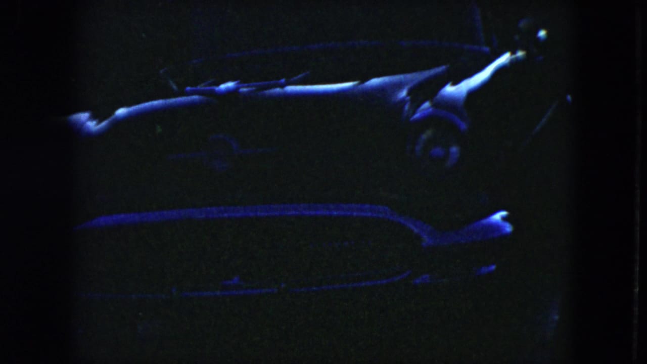 Low-light 1951 Cleveland home-movie frame showing a parked mid-century car with blue highlights across the hood, windshield, and chrome.