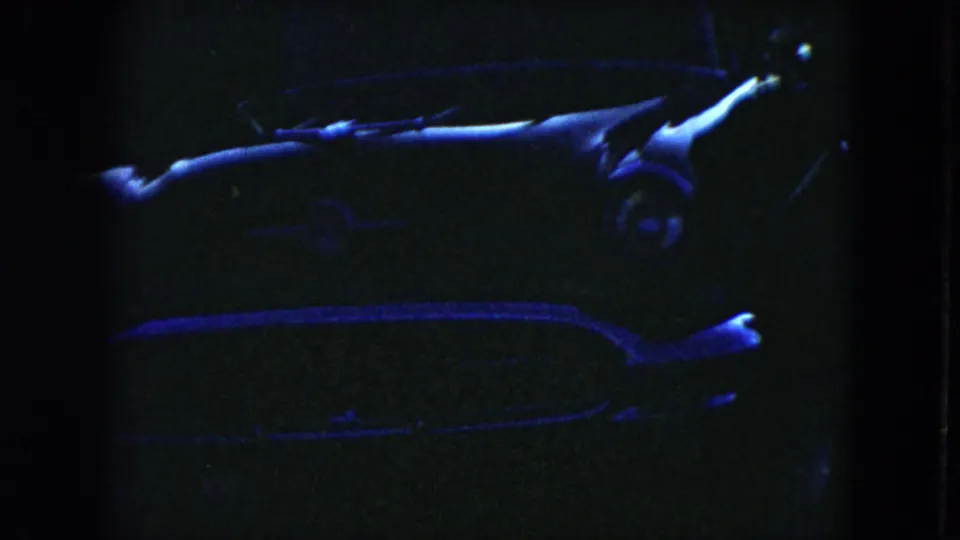 Low-light 1951 Cleveland home-movie frame showing a parked mid-century car with blue highlights across the hood, windshield, and chrome.