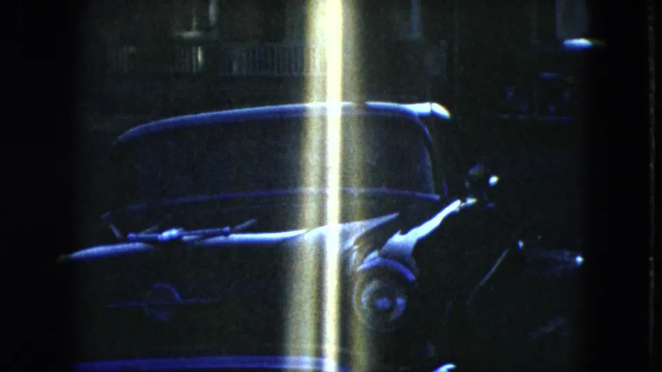 Low-light 1951 Cleveland frame showing the front of a parked sedan under a bright vertical flare.