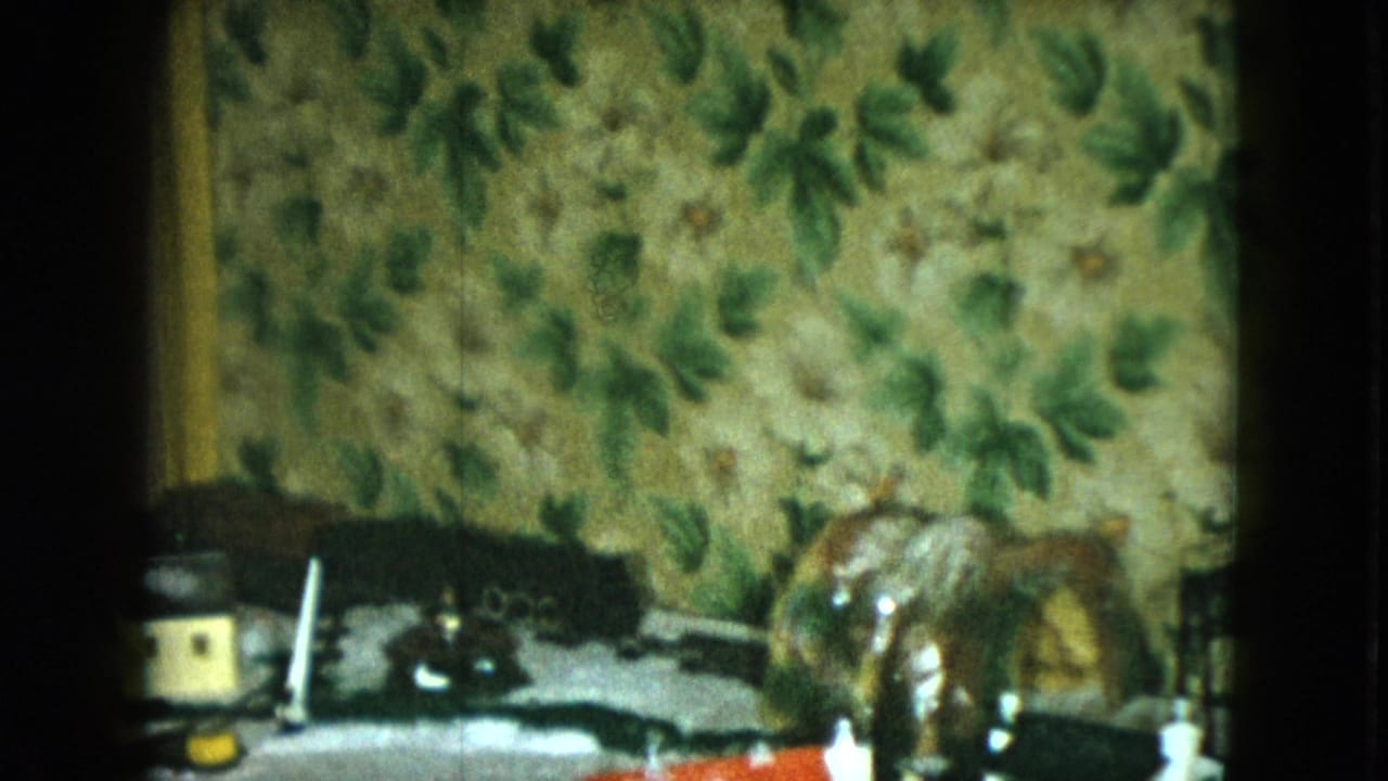 Miniature train scene with a toy house, horse figurine, track, and patterned wallpaper backdrop.