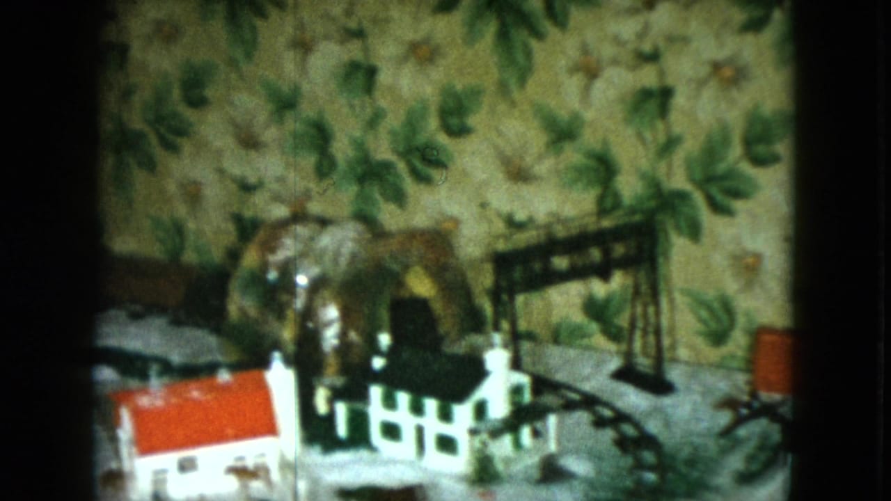 1951 Cleveland frame of a tabletop model train town with a red-roofed house, white fence, black bridge, horse figurine, and curved track.