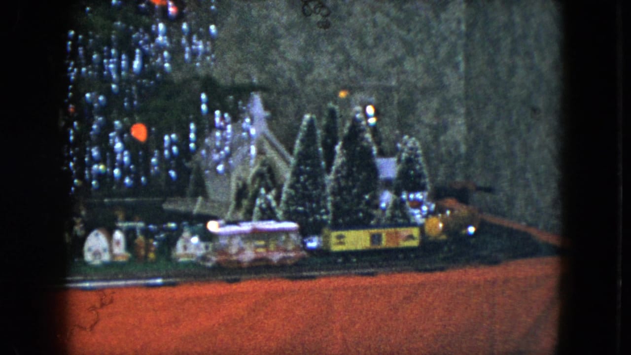 Model train beside miniature houses and snowy trees under Christmas lights.