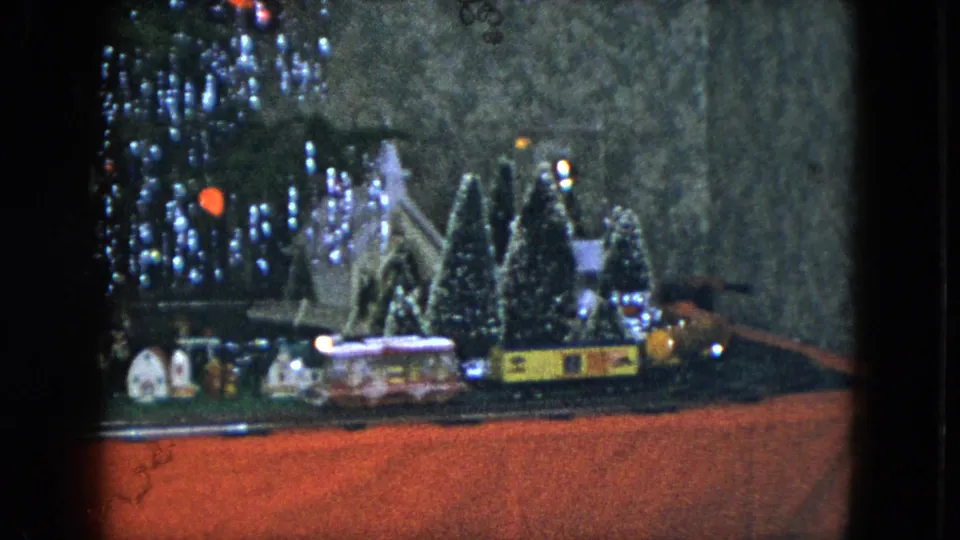 1951 Cleveland home-movie frame showing a model train passing a miniature winter village beneath a decorated Christmas tree.
