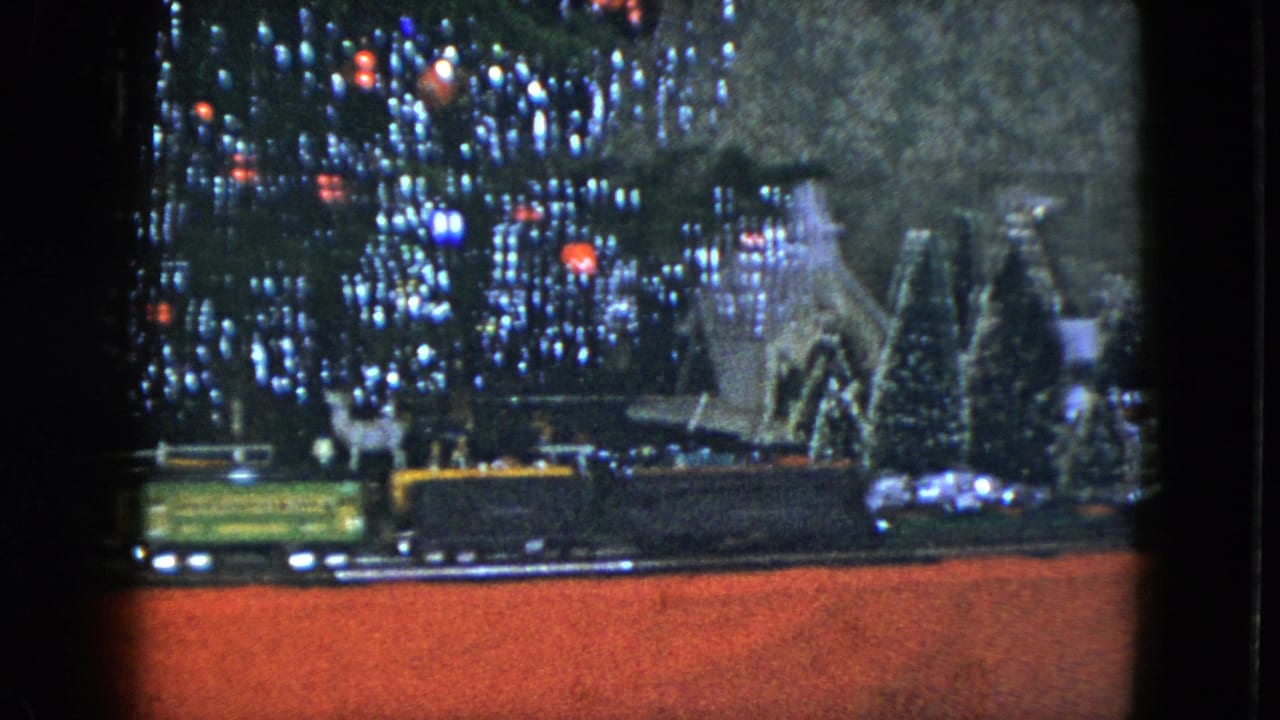 A green model train car and darker car travel along track beneath Christmas lights in the 1951 Cleveland holiday display.