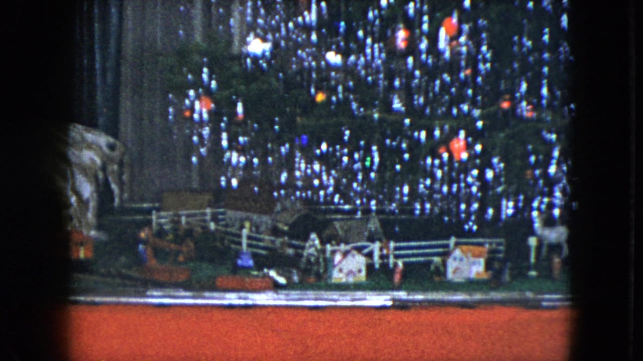 1951 Cleveland home-movie frame showing a tabletop model train scene beneath a lit, tinsel-covered Christmas tree.