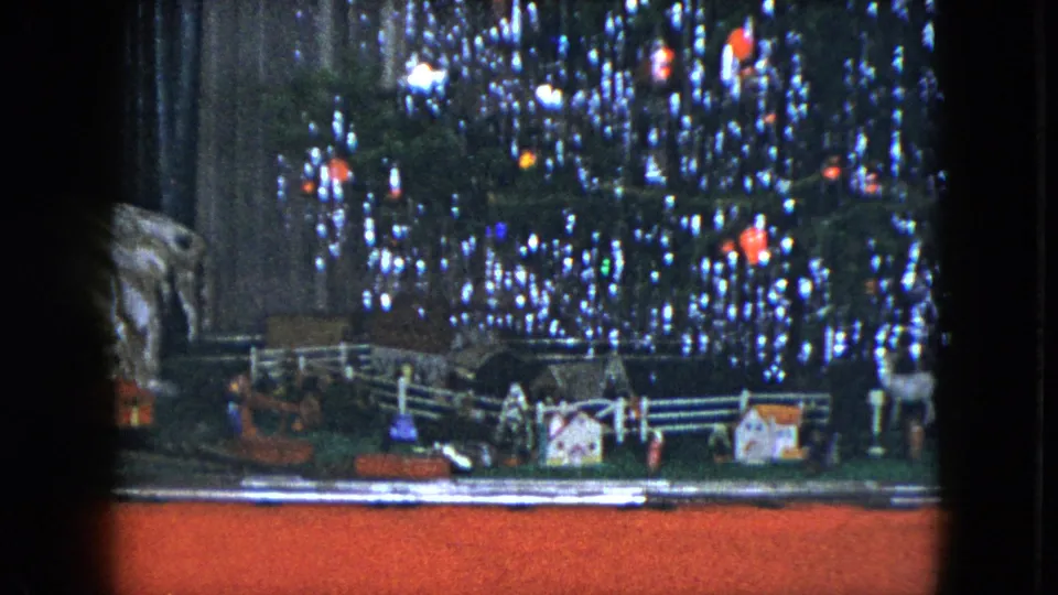 1951 Cleveland home-movie frame showing a tabletop model train scene beneath a lit, tinsel-covered Christmas tree.