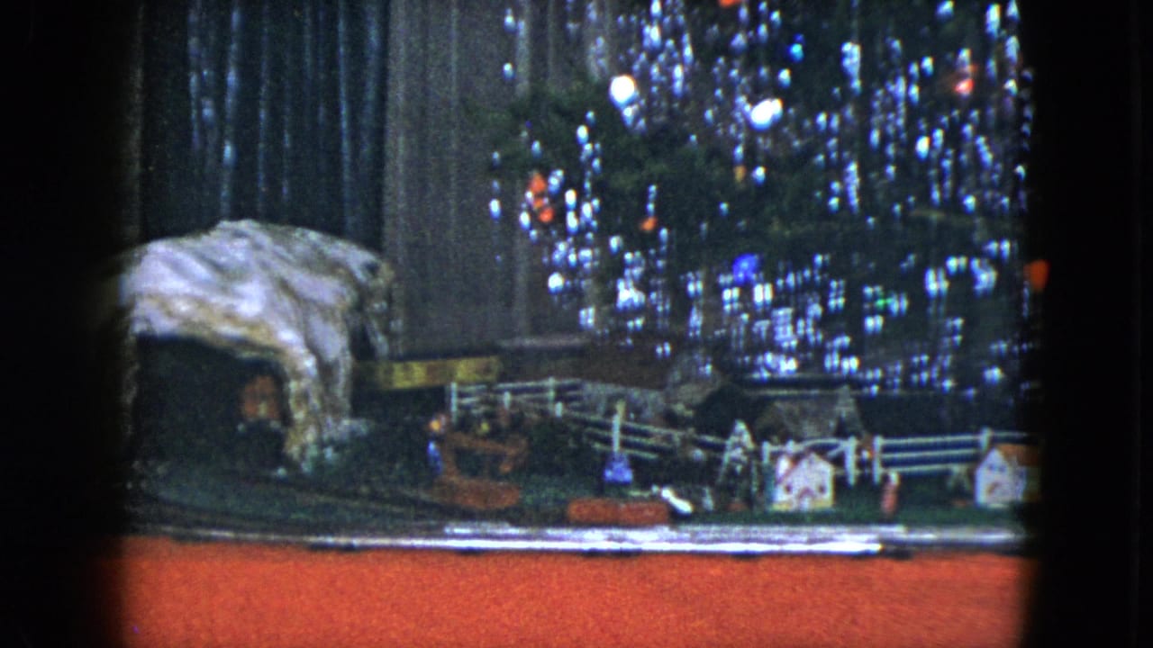 Miniature holiday village and train track in front of a lit Christmas tree.