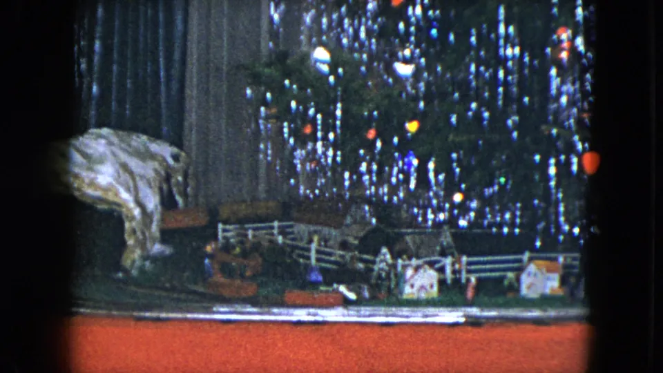 1951 Cleveland 8mm frame showing the train layout from a slightly shifted view, with miniature houses and a lit tinsel tree behind.