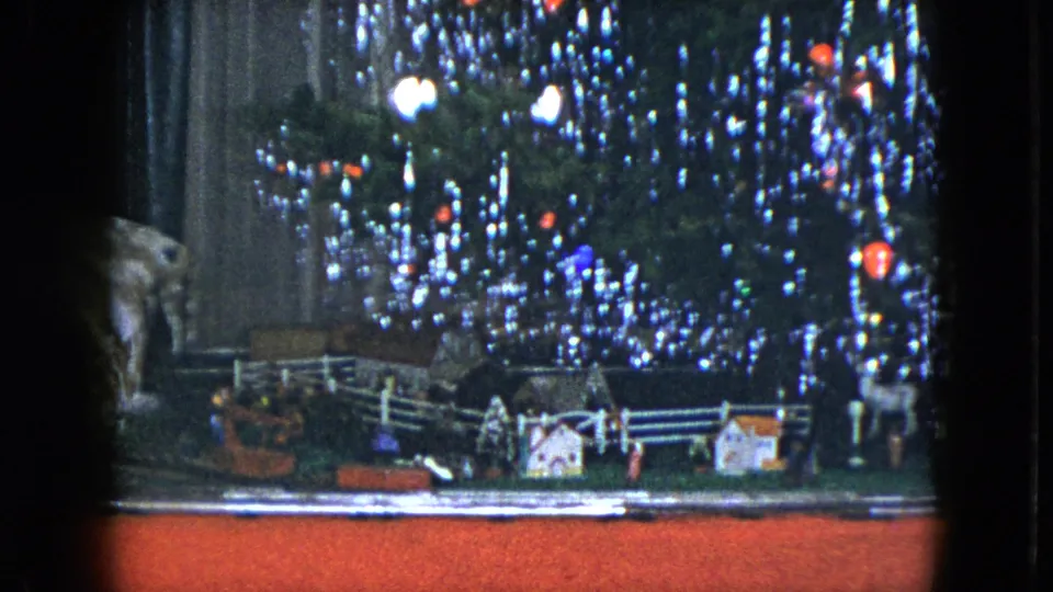 1951 Cleveland home-movie frame of a tabletop Christmas train display beneath a sparkling tree with colored bulbs and tinsel.
