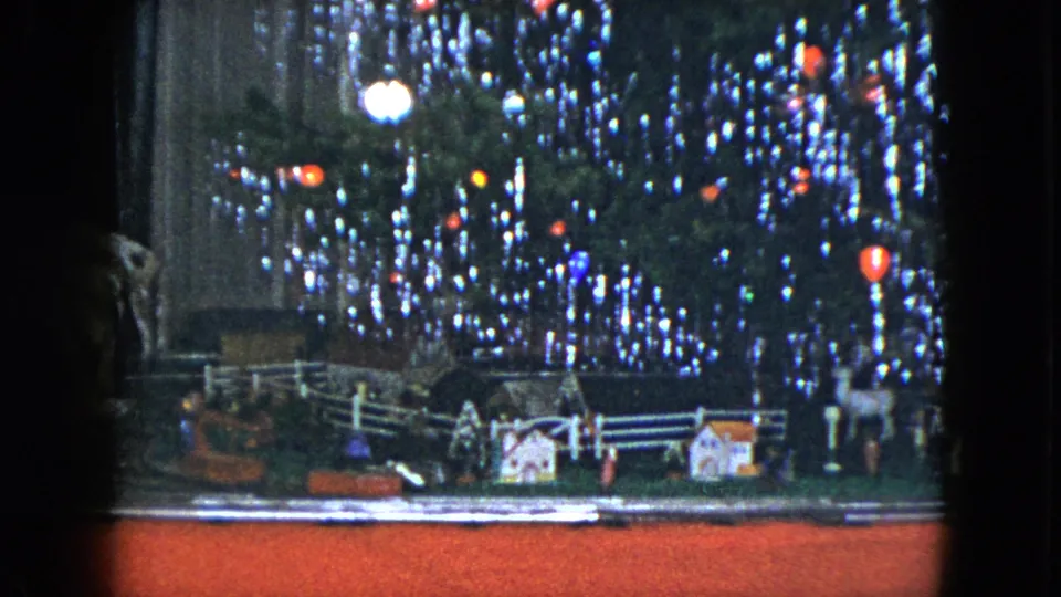 1951 Cleveland home-movie frame showing a small model train setup beneath a decorated Christmas tree.