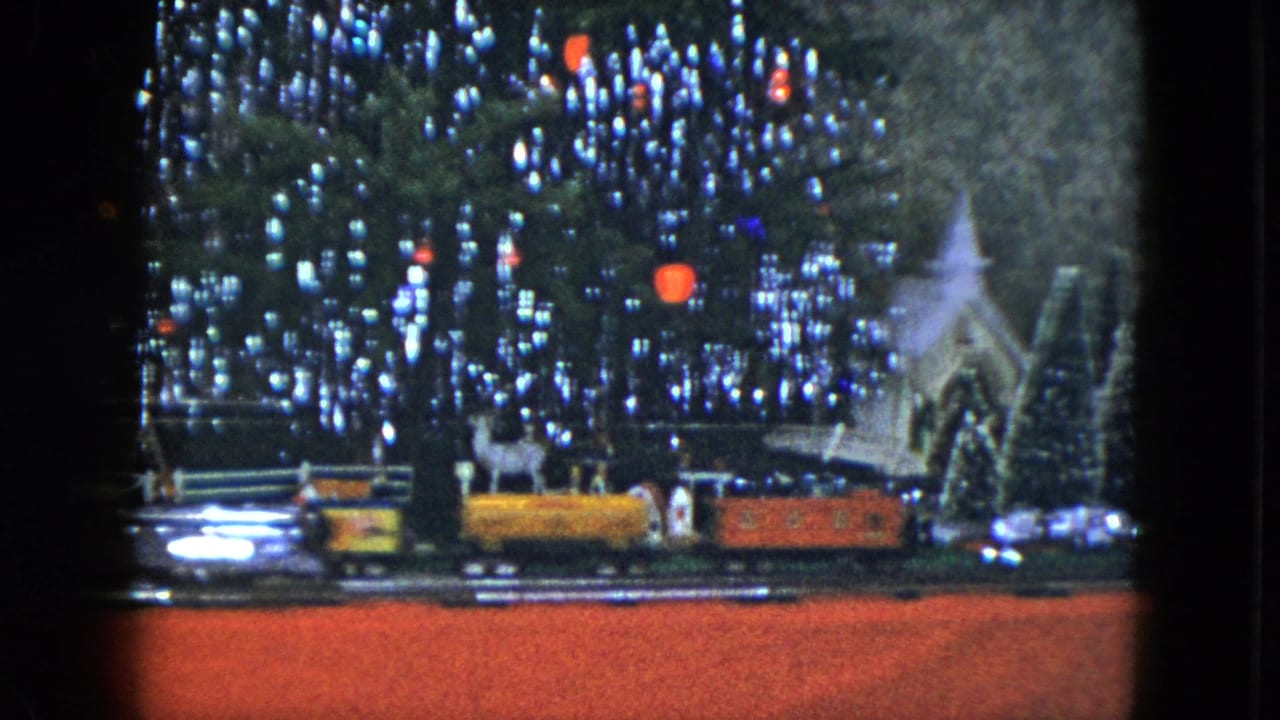 1951 Cleveland 8mm frame showing a model train, lit Christmas tree, miniature church, and red display floor in a holiday storefront scene.